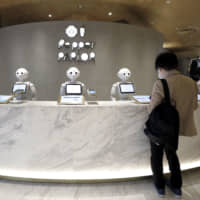 SoftBank Group Corp.\'s Pepper robots stand behind a counter while a customer places an order at the Pepper Parlor cafe in Tokyo on Thursday. The Tokyu Plaza Shibuya shopping complex housing SoftBank Robotics Group Corp.\'s robot-staffed cafe opened the same day. | BLOOMBERG