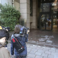 Members of the media wait outside the building housing the office of lawyer Junichiro Hironaka — one of the former lawyers for ex-Nissan Motor Co. Chairman Carlos Ghosn, who jumped bail and fled to Lebanon late last year — in Tokyo\'s Chiyoda Ward Wednesday as prosecutors search the office in connection with the case. | KYODO