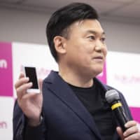 Hiroshi Mikitani, chairman and chief executive officer of Rakuten Inc., holds up a Rakuten Mini smartphone while speaking during a news conference in Tokyo on Sept. 6. | BLOOMBERG