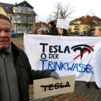 Demonstrators hold anti-Tesla posters during a protest against plans by U.S. electric vehicle pioneer Tesla to build its first European factory and design center in Gruenheide near Berlin Saturday. | REUTERS
