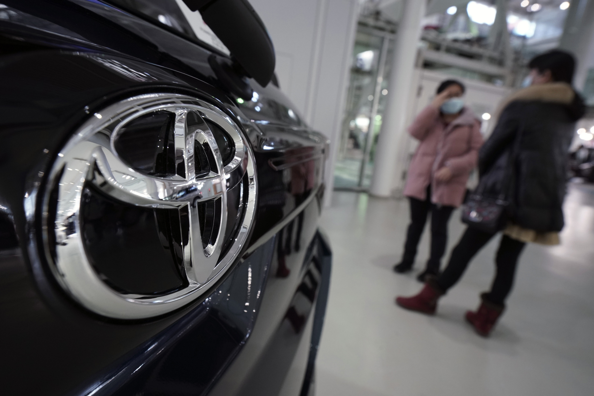 Visitors stand by a Toyota Motor Corp. car at a showroom on Thursday in Tokyo. German automaker Volkswagen AG has kept its lead as the world's largest automaker, selling more vehicles than Toyota last year. | AP