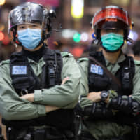 Riot police wear protective masks while standing guard on Nathan Street in the Mong Kok district of Hong Kong on Sunday. | BLOOMBERG