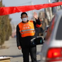 A village committee member on Wednesday stops a car in Tianjiaying village, on the outskirts of Beijing, as he guards the entrance of a community to prevent outsiders from entering amid the coronavirus outbreak. | REUTERS