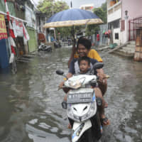 Residents ride a motorbike along a flooded street in Jakarta on Sunday. | AP