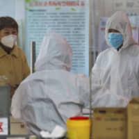 Medical workers in protective gear talk with a woman suspected of being ill with a coronavirus at a community health station in Wuhan in central China\'s Hubei Province Monday. | CHINATOPIX / VIA AP
