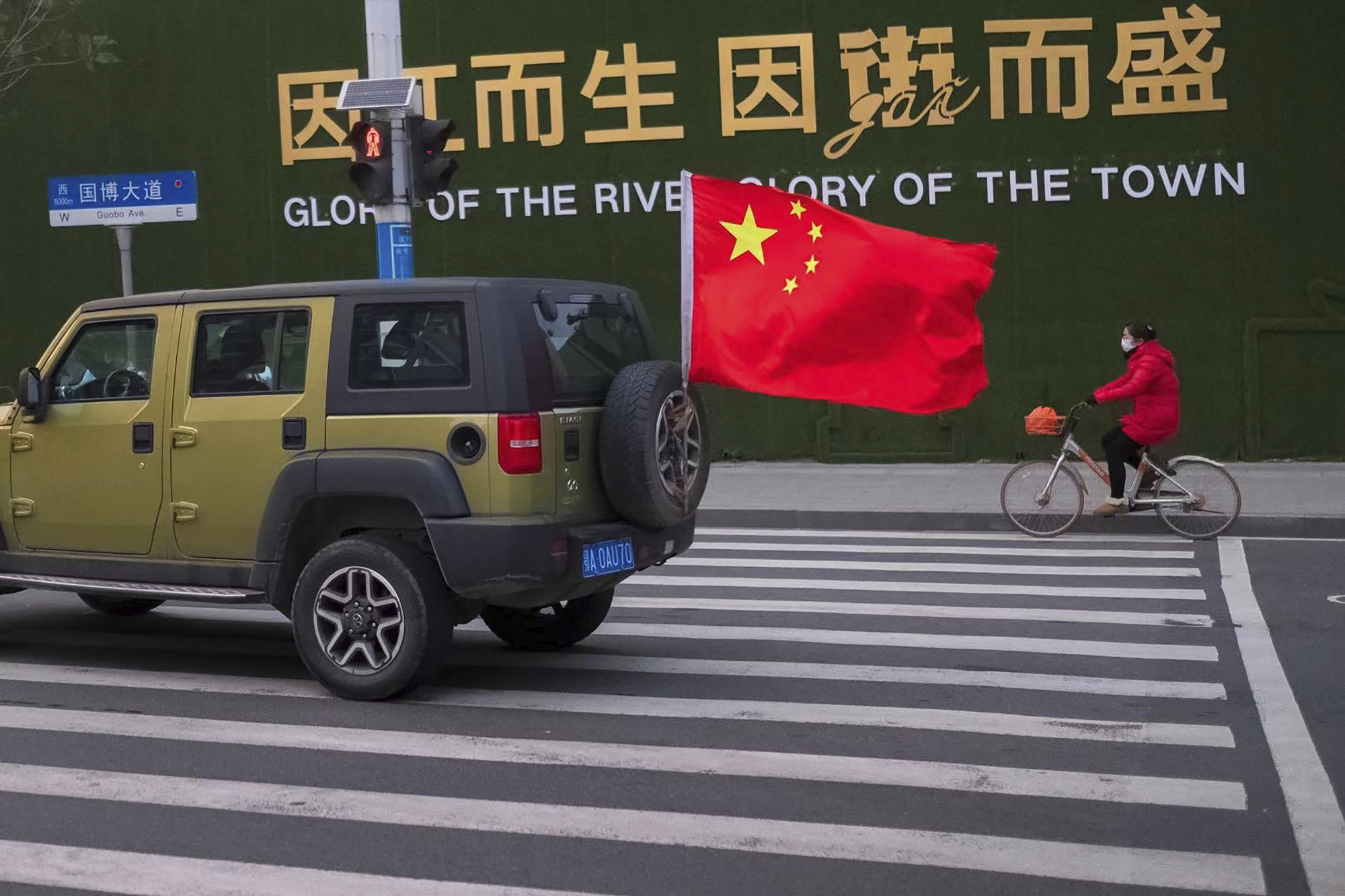 A vehicle flying a Chinese flag drives past a woman wearing a face mask as she rides a bicycle along a street in Wuhan in central China's Hubei Province Wednesday. Countries began evacuating their citizens Wednesday from the Chinese city hardest-hit by a new virus that has now infected more people in China than were sickened in the country by SARS. | AP