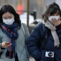 Two women wear surgical masks due to high levels of pollution in Milan, Italy, Wednesday. | REUTERS