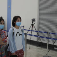 Chinese passengers wearing face masks walk past a thermal scanner set up to check the temperature of passengers at Colombo International airport in Colombo Saturday. | AP