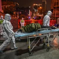 Medical staffers wearing protective clothing arrive with a coronavirus patient at the Wuhan Red Cross Hospital in the Chinese city on Saturday. | AFP-JIJI