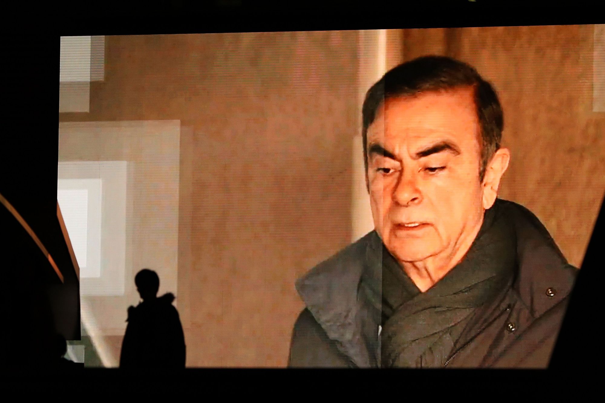 Pedestrians walk past a big TV monitor in Tokyo in April as Carlos Ghosn's image appears on a news program. Ghosn's stunning escape from Japan is bound to have an impact on future foreign suspects who seek to post bail, experts say. | PHOTOGRAPHER: TAKASHI AOYAMA/GETTY IMAGES