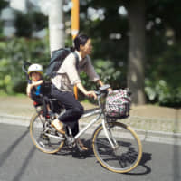 A woman takes her daughter to a day care facility in Tokyo. A recent government survey showed that a record 61 percent believe women should continue working after having a child. | KYODO