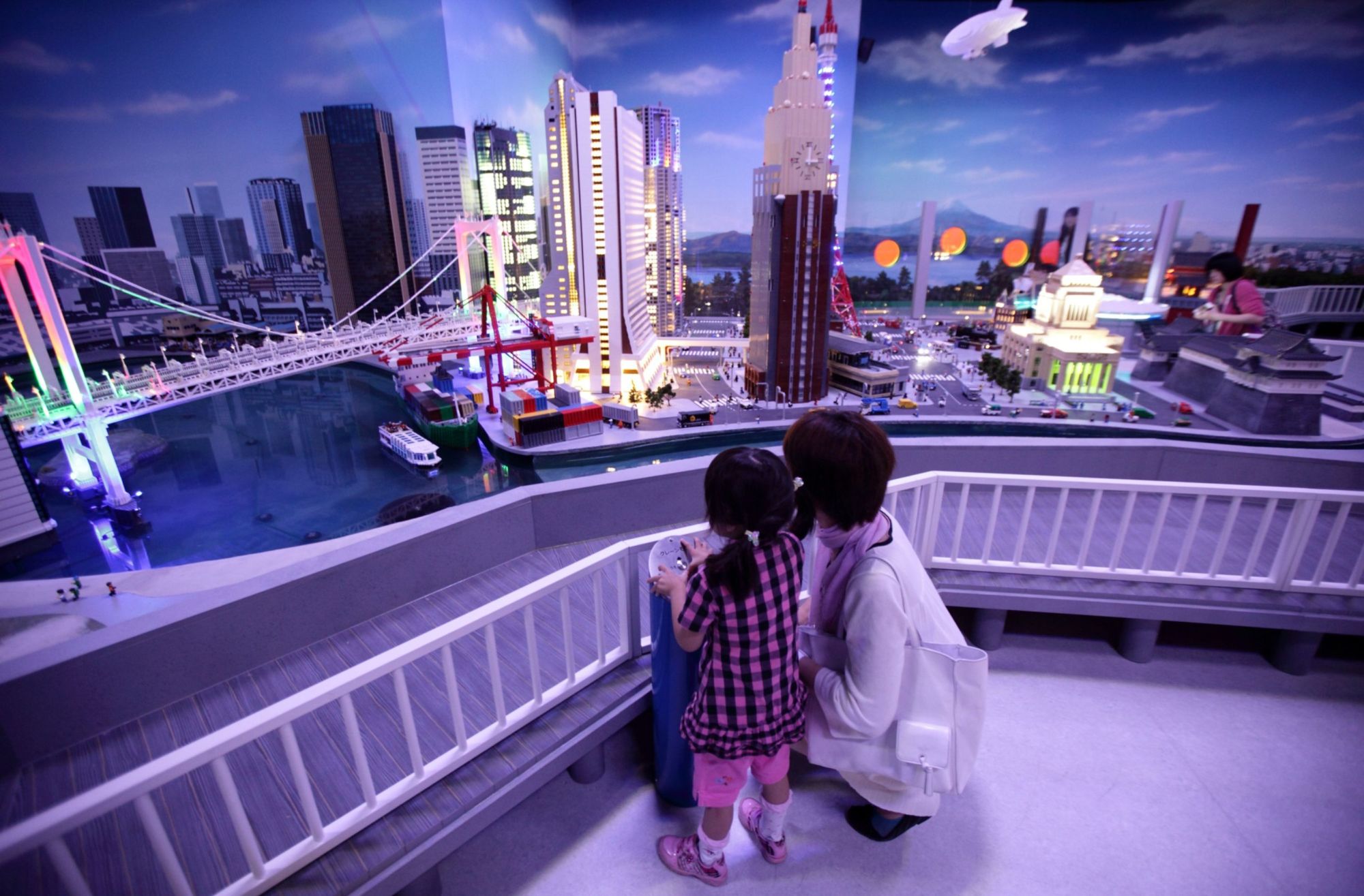 A child and her mother look at a diorama of Tokyo at night made by Lego A/S toy bricks at the Lego Land Discovery Center Tokyo in the capital in June 2012. A confluence of factors that include an aging population, falling birth rates and anachronistic gender dynamics are conspiring to damage women's prospects for a comfortable retirement. | BLOOMBERG