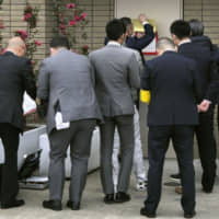 Police officers put up a notice on the wall of an office of Kodo-kai, a yakuza group belonging to the Yamaguchi-gumi syndicate, on Tuesday in Nagoya. It announces that Kodo-kai has been designated as a yakuza group at war with other crime organizations. | AICHI PREFECTURAL POLICE / VIA KYODO