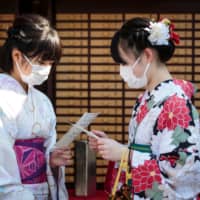Women in kimono wear face masks to help prevent the spread of the SARS-like Wuhan coronavirus as they read their fortunes at Sensoji Temple in Tokyo on Monday. | AFP-JIJI