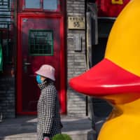 A woman wearing a protective facemask to protect against the COVID-19 coronavirus walks on a street in Beijing on Sunday. The coronavirus epidemic that has killed over 2,400 people is communist China\'s \"largest public health emergency\" since its founding, said President Xi Jinping on Sunday. | AFP-JIJI