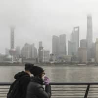 A couple walk in Shanghai on Friday. Broad policy direction for the world\'s central banks will hinge on how the Chinese government responds to the coronavirus outbreak. | BLOOMBERG