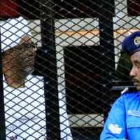 Sudan\'s jailed former president, Omar Hassan al-Bashir, sits inside a cage during a court hearing in Khartoum in December. | REUTERS