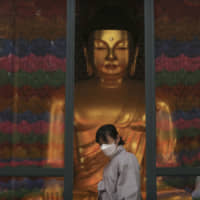 A Buddhist believer wearing a face mask leaves the Jogyesa Buddhist temple in Seoul on Tuesday. Countries around the world are stepping up efforts to prevent a pandemic of the flu-like coronavirus that originated in China late last year and has now infected more than 80,000 people as of Tuesday, 10 times more cases than SARS. | AP