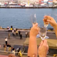 Passengers cheer and clink wine glasses as the MS Westerdam cruise ship docks at port in Sihanoukville, Cambodia, Thursday in this still image obtained from social media video. | ANGELA JONES / VIA REUTERS