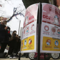People wearing face masks pray near posters warning about the coronavirus at the Jogyesa Buddhist temple in Seoul on Sunday. | AP