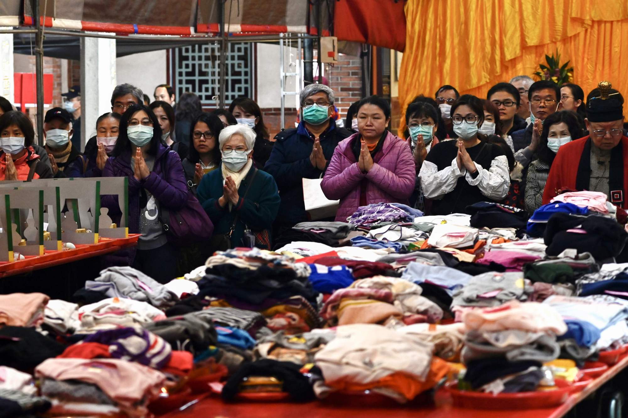 People wearing protective masks pray beside their clothes laid out on a table at a Taoist Baoan temple in Taipei on Tuesday. | AFP-JIJI