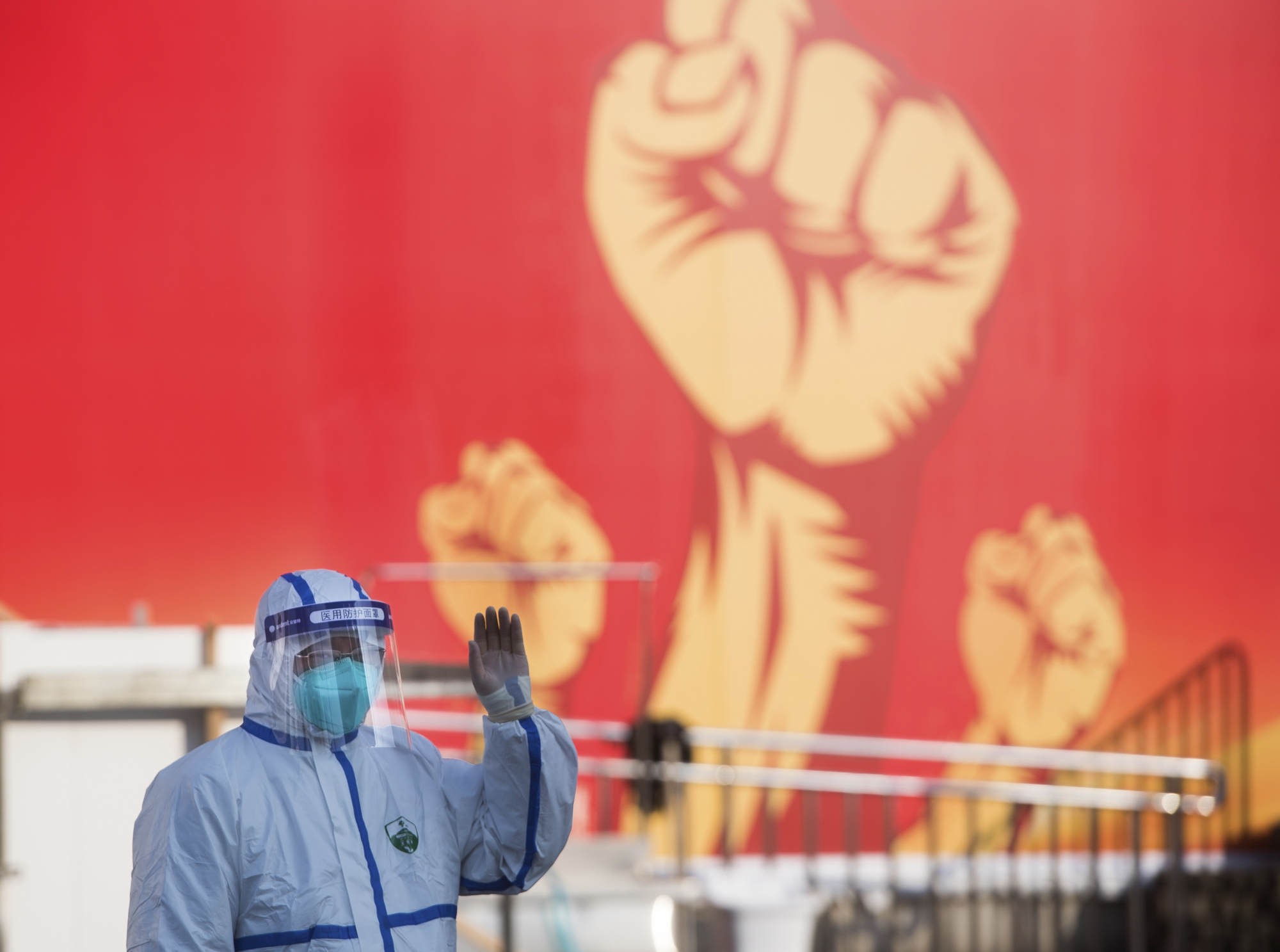 A medical worker waves near a propaganda poster as patients arrive at a temporary hospital converted from the Wuhan Sports Center in central China's Hubei Province on Wednesday. | AP