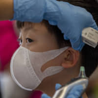 A health worker checks the temperature of tourist from Wuhan, China, as he waits for a charter flight back to the Chinese city at the Suvarnabhumi Airport in Bangkok on Friday. | AP