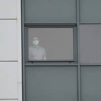A man stands at a window of a staff accommodation block where Britons recently flown back from China and at risk from the new virus are being quarantined at Arrowe Park Hospital in Liverpool, England, on Wednesday. Britain on Tuesday urged all of its citizens in China to leave the country because of the outbreak of a respiratory illness from a new virus. | AP
