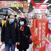 Chinese tourists walk past face masks on sale at an electronics store in Tokyo\'s Akihabara district on Jan. 27. | KYODO