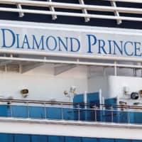 A passenger wearing a mask stands on the deck of the cruise ship Diamond Princess, as the vessel\'s passengers continue to be tested for the COVID-19 coronavirus at Daikoku Pier Cruise Terminal in Yokohama on Thursday. | REUTERS