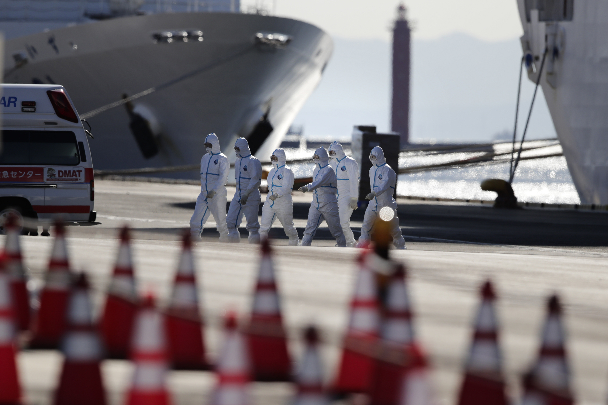 Medical workers with protective suites walk away from the quarantined Diamond Princess cruise ship in Yokohama on Tuesday. | AP