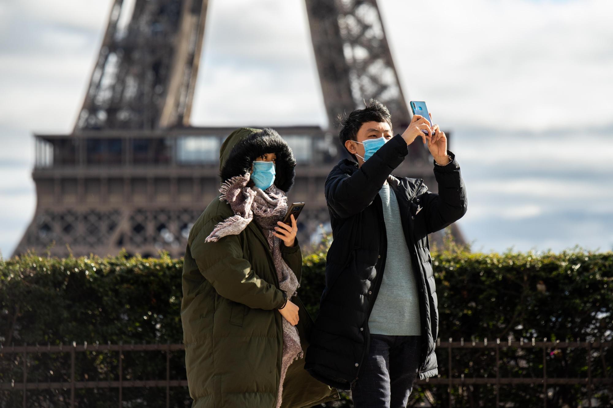 Tourists wearing protective face masks take a photo in front of the Eiffel Tower in Paris. | KYODO