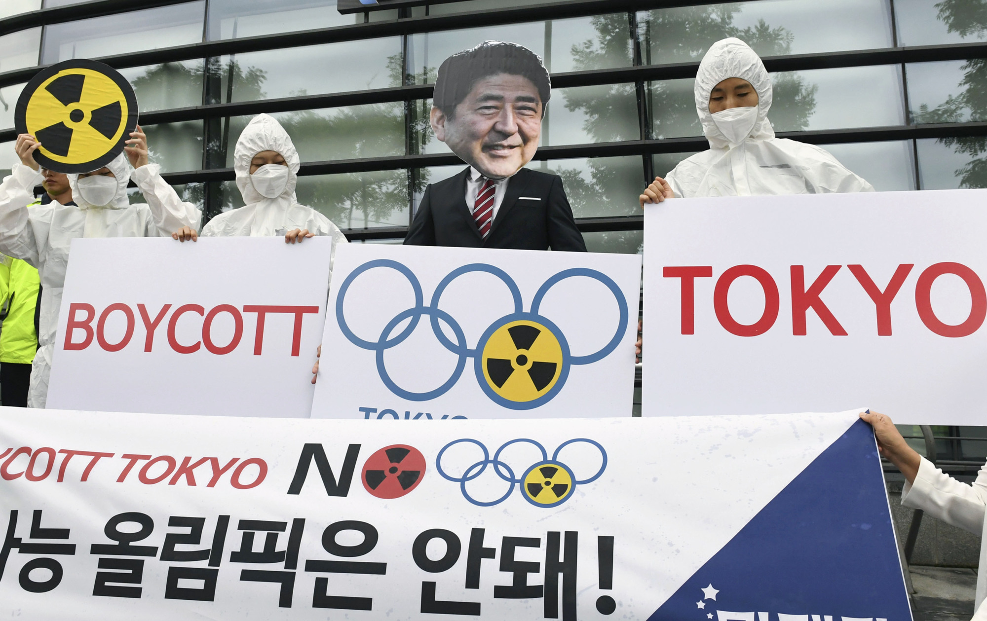 People in protective gear gather in front of the Japanese Embassy in Seoul on Aug. 7, 2019, calling for a boycott of the 2020 Tokyo Olympics, citing the need to protect athletes from exposure to radioactive substances released in the wake of the 2011 Fukushima nuclear crisis. | KYODO