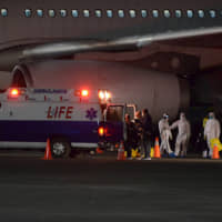 Philippine Department of Foreign Affairs and Department of Health members wear protective suits as they assist Filipinos from the Diamond Princess cruise ship as they arrive at the Clark Airbase, in Pampanga, Philippines, early Wednesday. | DFA / VIA AP