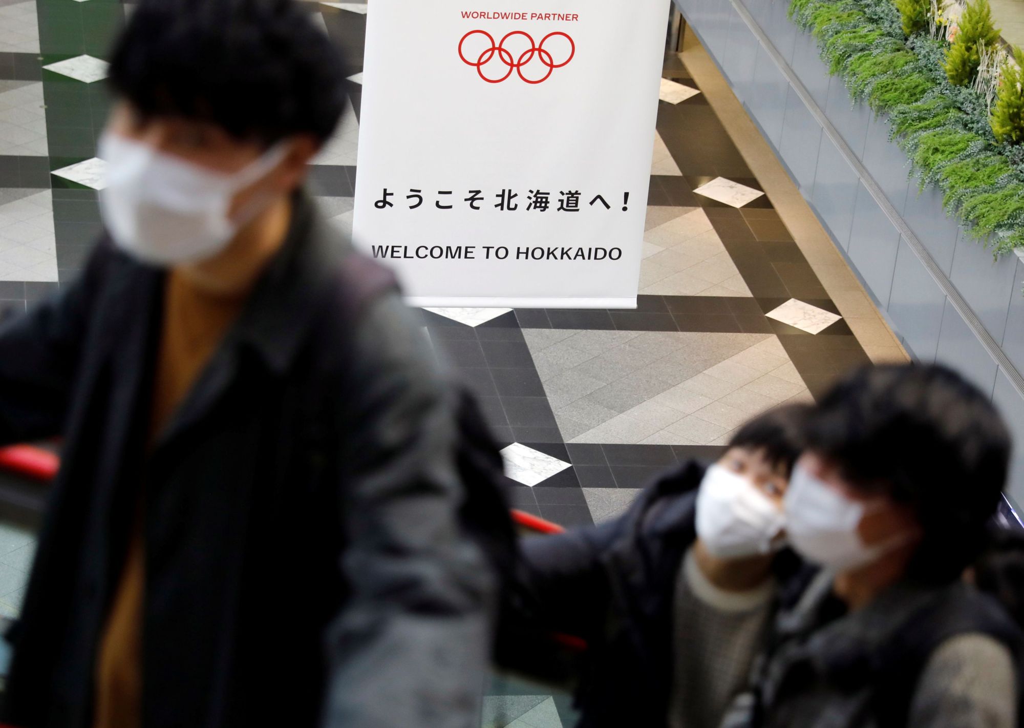 Passengers wearing protective face masks due to the coronavirus outbreak pass a banner for the Tokyo 2020 Olympic Games at New Chitose Airport in Chitose, Hokkaido, on Thursday. | REUTERS
