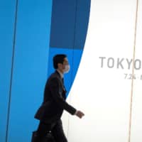 A man wearing a protective mask walks past a Tokyo 2020 billboard near Shinjuku Station in Tokyo. With Friday marking exactly 147 days until the opening ceremony for the Olympics on July 24, a scene from the 1988 post-apocalypse anime \"Akira\" has become a talking point on social media. | REUTERS