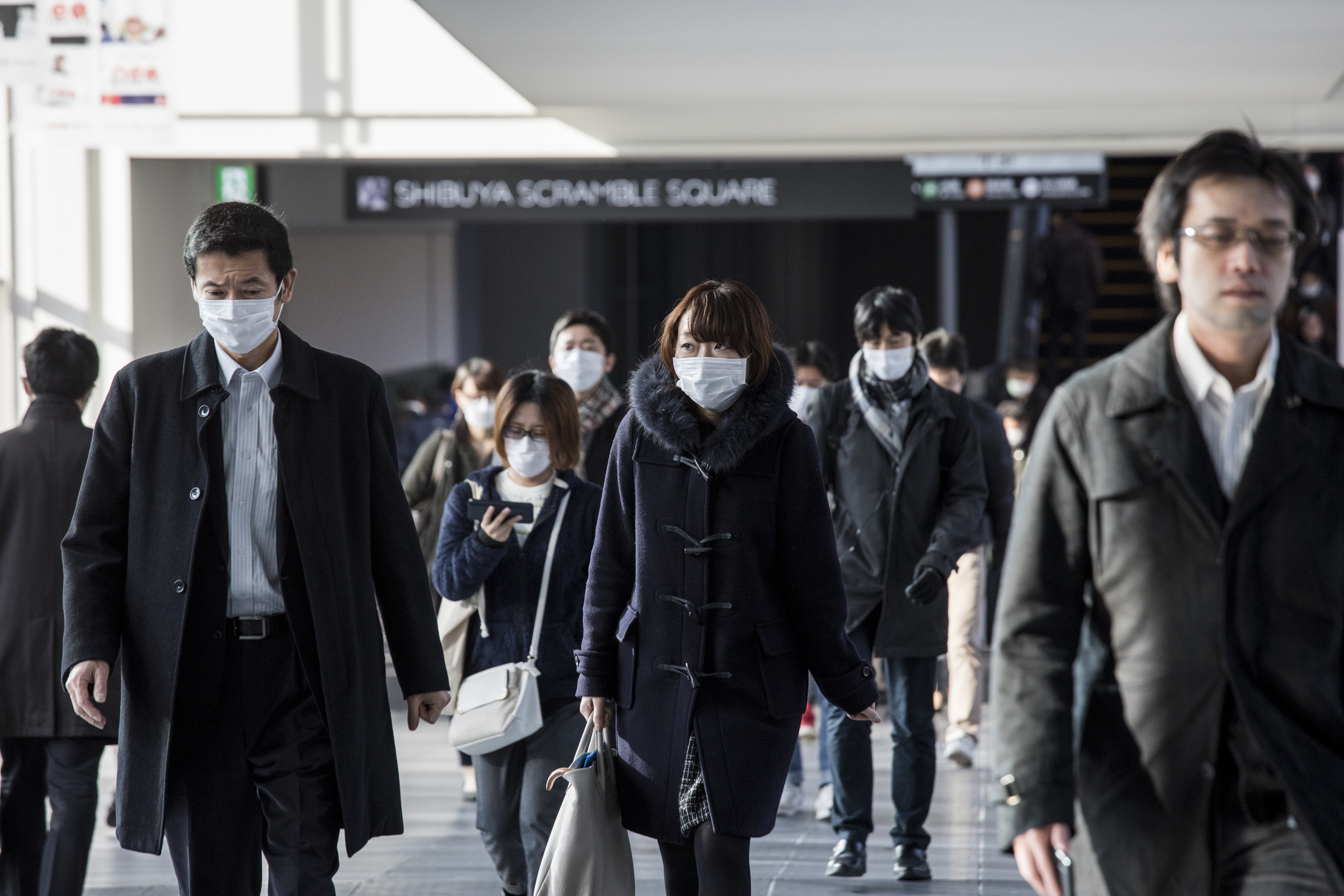 Morning commuters wearing protective masks walk through Tokyo’s Shibuya district. | BLOOMBERG