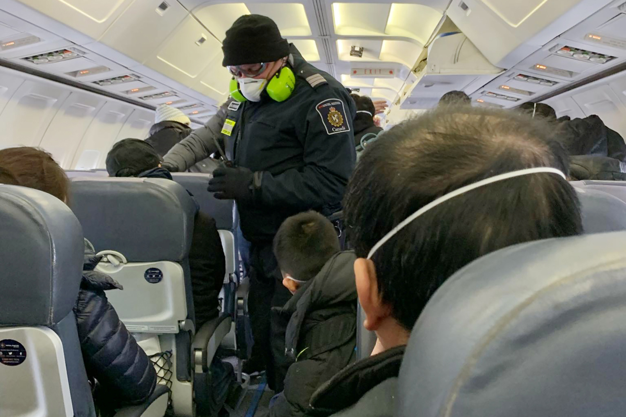 A Royal Canadian Mounted Police officer checks citizens being flown to Canadian Forces Base Trenton in Ontario on Friday after they were evacuated from China. | COURTESY OF EDWARD WANG / VIA REUTERS