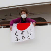 A woman unfolds a Japanese flag that reads \"shortage of medicine\" on the Diamond Princess cruise ship on Friday. The cruise liner is currently quarantined in the port of Yokohama as a result of the coronavirus. | REUTERS