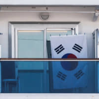 A South Korean flag is seen on the balcony of a cabin on the cruise ship Diamond Princess, as the vessel\'s passengers continue to be tested for coronavirus, at Daikoku Pier Cruise Terminal in Yokohama, on Thursday. | REUTERS