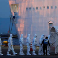 Officers in protective gear enter the cruise ship Diamond Princess on Friday to take a coronavirus patient to the hospital after its arrival in Yokohama. The government plans to announce tourism-support measures against the global outbreak later this week. | REUTERS