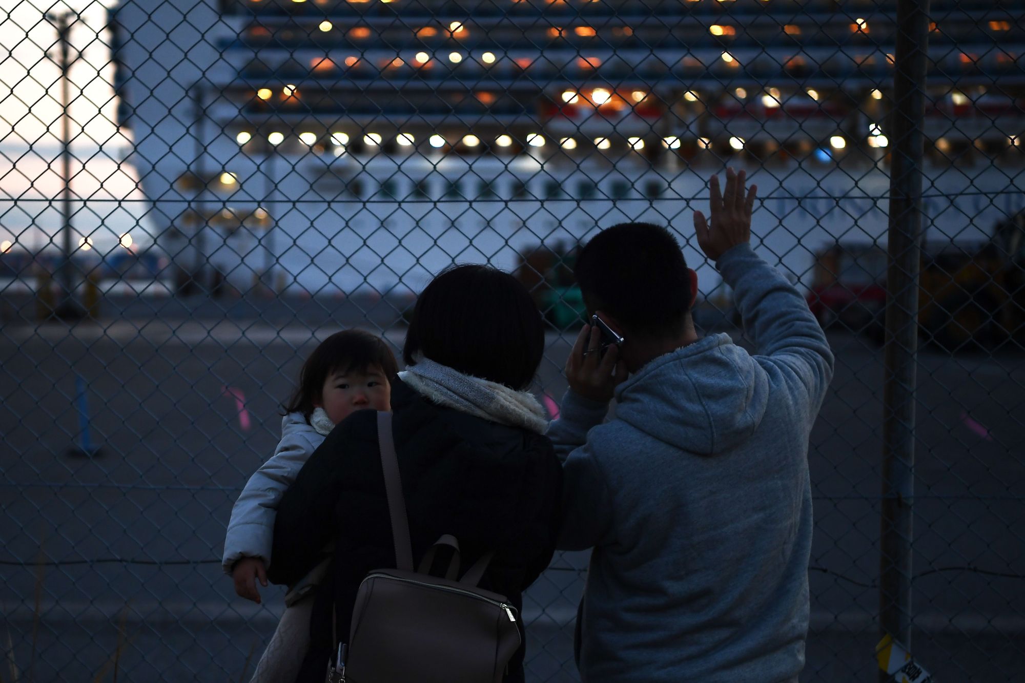 Relatives of passengers watch the Diamond Princess as it sails from Daikoku Pier Cruise Terminal in Yokohama on Tuesday to spend a day at sea dumping wastewater and generating drinking water. | AFP-JIJI