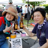 Grains for good: Yoko Higuchi (right) and another volunteer kick back with an official 2019 Soma Tambo Art Project  beer at a summer viewing party. | COURTESY OF THE SOMA TAMBO ART PROJECT