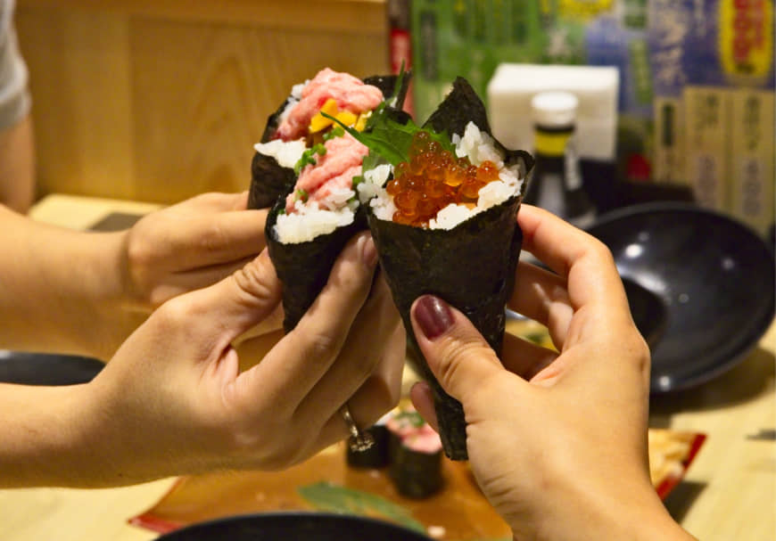 Tasting the best of Japan: Arigato Japan Food Tours participants hold up colorful, seafood-laden temaki (sushi hand roll). | CREATIVE COLLECTIVE