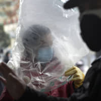Fear factory: A man wearing a plastic bag over his head enters a supermarket in the central Chinese city of Wuhan, the epidemic\'s ground zero, on Feb. 10. | AP