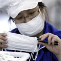 Protective gear: An employee inspects a face mask at a factory in Toyohashi, Aichi Prefecture. Face masks are becoming hard to come by in Japan as fears over CORVID-19 persist. | BLOOMBERG