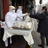 A restaurant worker wearing protective clothing as a preventive measure against COVID-19 passes a bag of food to a customer on the street outside a restaurant in Beijing on Feb. 20. | AFP-JIJI