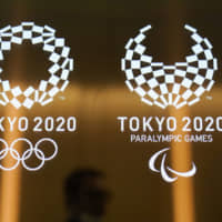 A man walks past the logos for the 2020 Tokyo Olympics and Paralympics on June 11, 2019. | AP