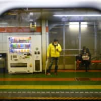 A man, wearing a protective face mask, following an outbreak of the COVID-19 virus, looks on his mobile phone inside a subway station in Tokyo. A 44-year-old man in Shimane Prefecture has been arrested after he pretended to have contracted the virus and threatened to spread it at a local train station, NHK reported Saturday. | REUTERS