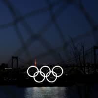 The giant Olympic rings are seen in the dusk through a steel fence at the waterfront area at Odaiba Marine Park after postponing Games due to the outbreak of coronavirus disease in Tokyo on March 25. | REUTERS